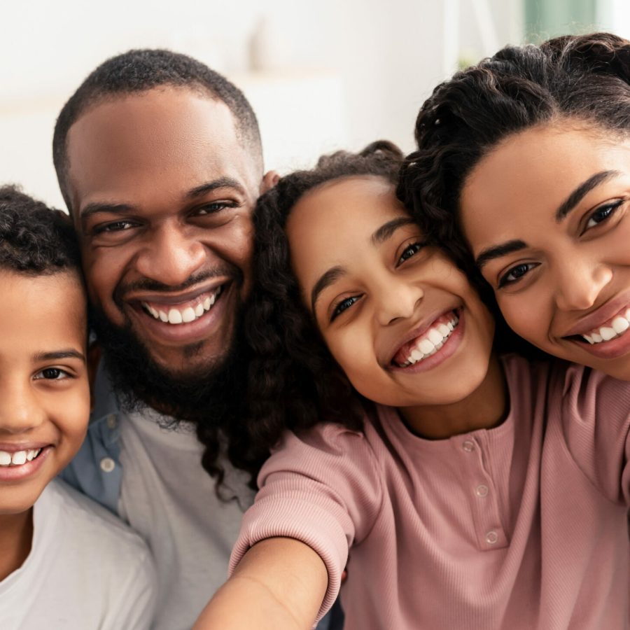 Capturing Moments. Portrait of happy loving black family of four people taking selfie together, closeup. Positive parents posing with their kids and smiling, girl holding camera, pov